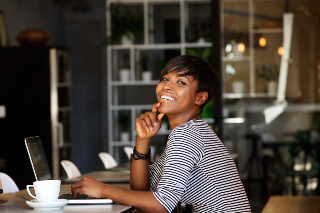 ChigisWorld Side portrait of a smiling young african american woman sitting at cafe with laptop